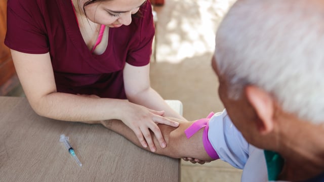 Rural nurse looking for the vein in the arm of a senior male patient.