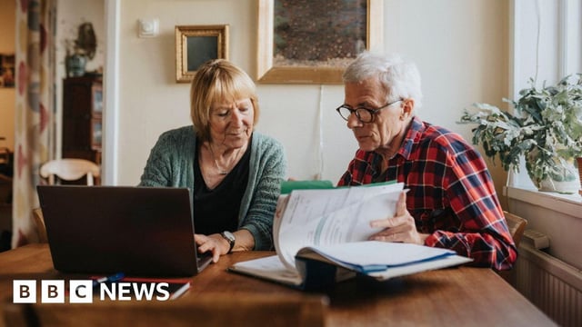 Pensioner couple look through their finances on paper and a laptop
