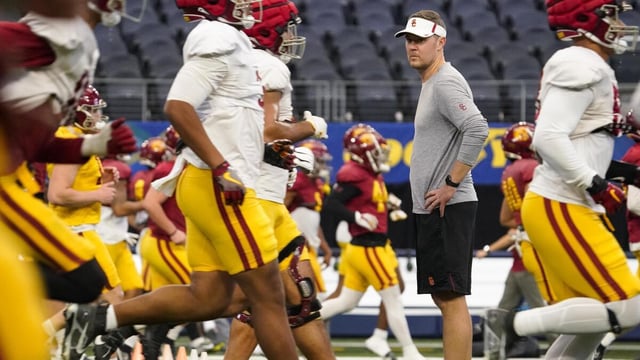 USC coach Lincoln Riley stands on the field and  watches his team warm up around him