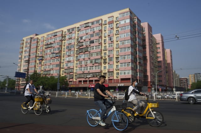 Chinese riding bicycle pass by a local business building the in background in Beijing, China, Friday, June 28, 2024. Surveys of Chinese factory managers showed a mixed outlook for the world's second-largest economy in June, with growth steady but not picking up much steam. (AP Photo/Vincent Thian)