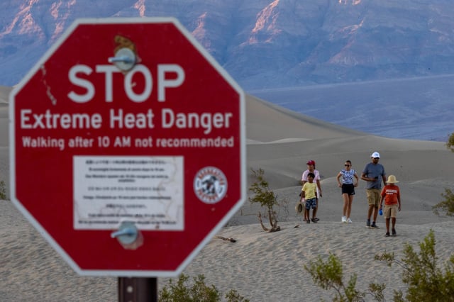 FILE: People walk among sand dunes near a sign warning of extreme heat danger on the eve of a day that could set a new world heat record in Death Valley National Park on July 15, 2023, near Furnace Creek, Calif.