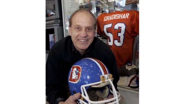 FILE - Former Denver Broncos linebacker Randy Gradishar holds one of his football helmets as he sits in front of a trophy case full of memorabilia from his playing days at an automobile dealership in Lakewood, Colo., Jan. 31, 2008. Gradishar, Steve McMichael and Art Powell are finalists for the Pro Football Hall of Fame's class of 2023. The three were picked as the three senior candidates from a list of 12 semifinalists.(AP Photo/Ed Andrieski, File)