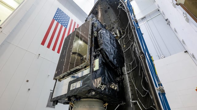 closeup photo of a satellite inside its rocket's payload fairing, inside a white-walled assembly building