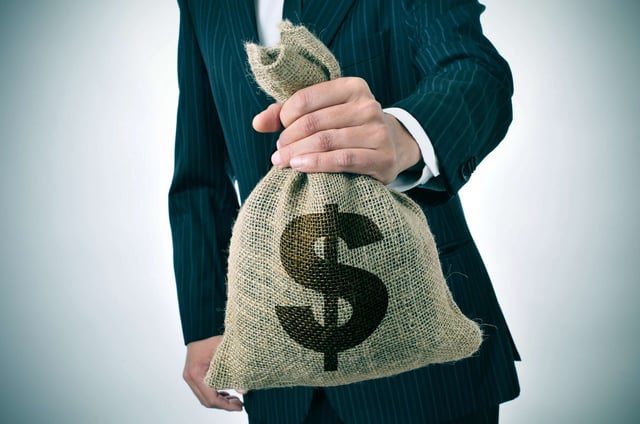 A man in a suit holds a burlap sack with a dollar sign on it