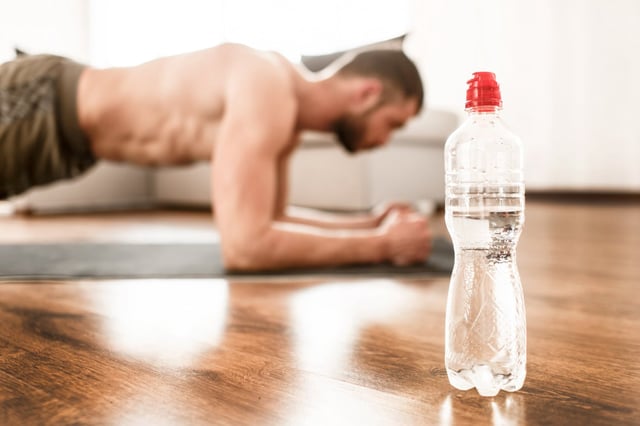 Water bottle close-up. Young man doing sport at home
