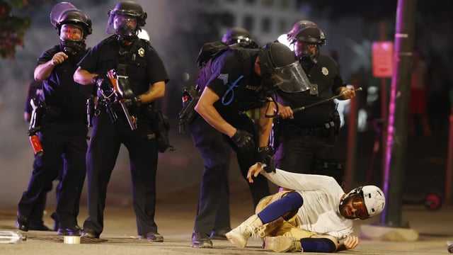 FILE - Denver Police Department officers clear a man who fell to the street after they used tear gas and rubber bullets to disperse a protest outside the Colorado Capitol in Denver, May 28, 2020, over the death of George Floyd. Denver will pay $4.7 million to settle a class action lawsuit that alleged that protesters were unjustly targeted for violating the city's curfew during demonstrations over the killing of Floyd in 2020. City councilors unanimously agreed to the deal Monday, Aug. 28, 2023, without any debate. (AP Photo/David Zalubowski, File)