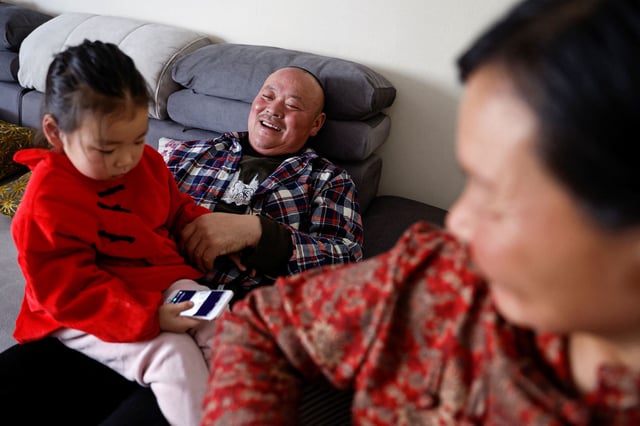 Wu Yonghou, 58, rests with his granddaughter sitting on his lap, next to his wife Yang Chengrong, 60, after a meal on Chinese Lunar New Year's Eve, at their apartment in a town bordering Beijing, in Hebei province, China February 9, 2024. REUTERS/Tingshu Wang