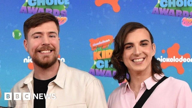 MrBeast pictured with Ava Kris Tyson at the Nickelodeon Kids Choice Awards. MrBeast has short brown hair and a short beard and wears a white overshirt over black T-shirt. Ava has shoulder-length brown hair parted to the side and wears a pink shirt.
