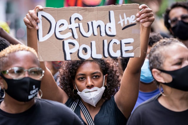 A protester wears a mask and holds a homemade sign that says, "Defund the Police" during a peaceful protest walk across the Brooklyn Bridge on June 19, 2020.