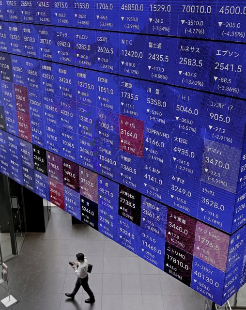 A person walks below an electronic stock board in Tokyo Thursday, July 25, 2024. Asian shares mostly declined in cautious trading Tuesday, July 30, ahead of central bank meetings around the world. (Kyodo News via AP, File)