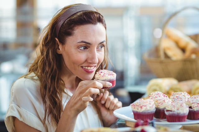 Pretty brunette holding and smelling cupcake in the bakery store