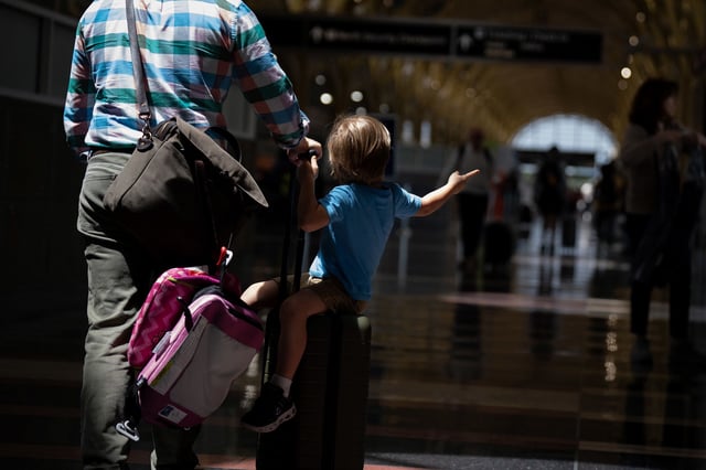 A boy sits on a rolling suitcase as travelers make their way through Ronald Reagan Washington National Airport in Arlington, Virginia on May 24, 2024.