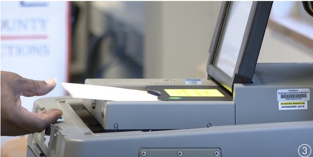 A voter loads a ballot into a voting machine.