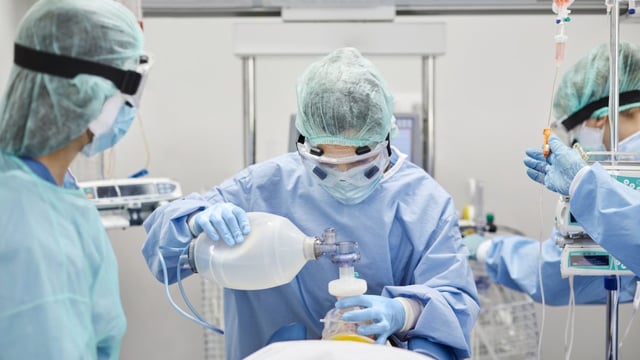 A patient being intubated in the ICU by 3 nurses dressed in PPE