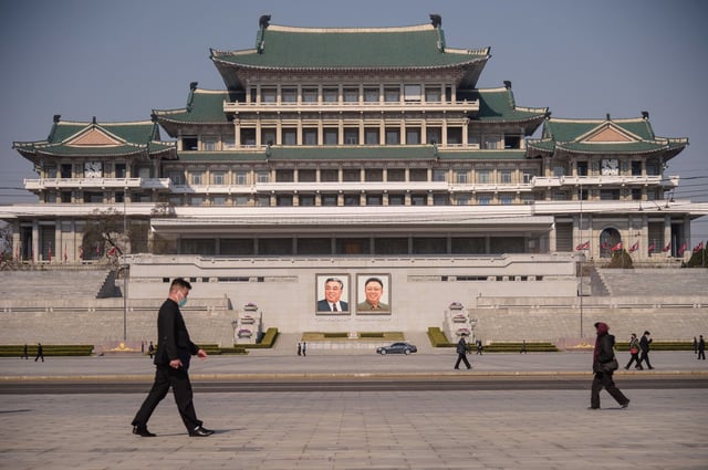 People wearing face masks walk before the portraits of late North Korean leaders Kim Il Sung and Kim Jong Il (centre R) on Kim Il Sung Square in Pyongyang on April 9, 2020. (Photo by KIM Won Jin / AFP) (Photo by KIM WON JIN/AFP via Getty Images)