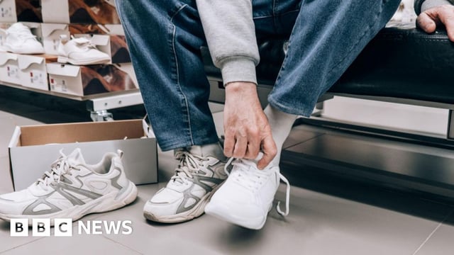 Man trying on white trainers in shoe shop
