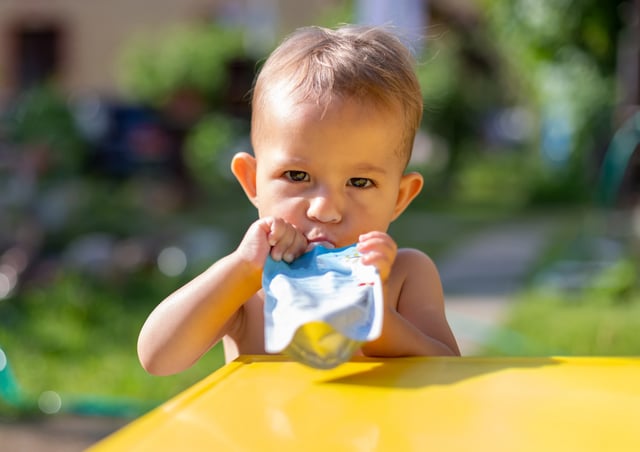 Serious baby eating fruit puree in pouch