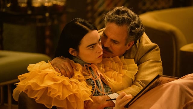 A woman in a ruffled dress is embraced by her male lover in a scene from the movie "Poor Things."