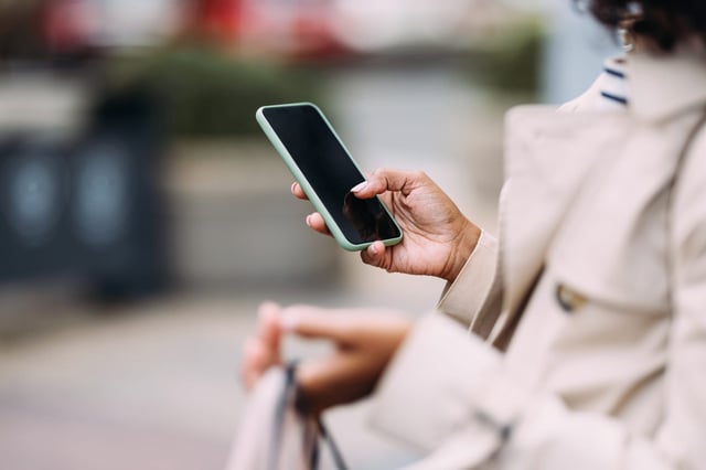 Close-up shot of a hand holding a smartphone outdoors, depicting modern communication and technology use in everyday life.