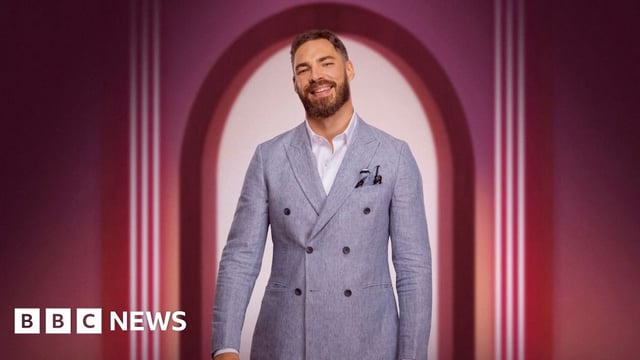 Publicity shot featuring Steven Smith in a grey jacket and white shirt smiling at the camera, framed by a pink archway