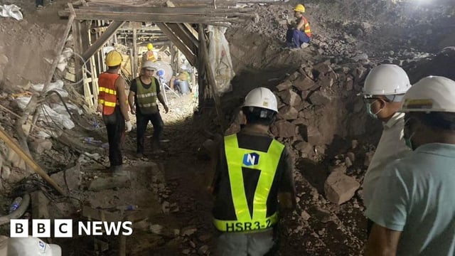 Rescue workers, wearing white helmets and florescent jackets, dig through a tunnel looking for the trapped workers