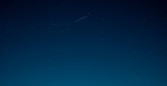 A view of point stars in the evening sky with a bright streak of light near the top of the photo.