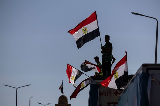 Volunteers carry Egyptian flags as they wait with aid convoy trucks loaded with supplies near the North Sinai Governorate building on October 15, 2023 in North Sinai, Egypt.
