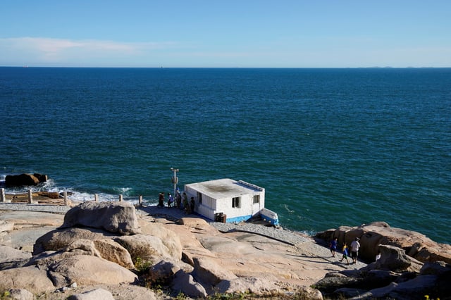 People stand near a building overlooking the Taiwan Strait, at the 68-nautical-mile scenic spot, one of mainland China's closest points to the island of Taiwan, in Pingtan island, Fujian province, China August 5, 2022. REUTERS/Aly Song/File Photo