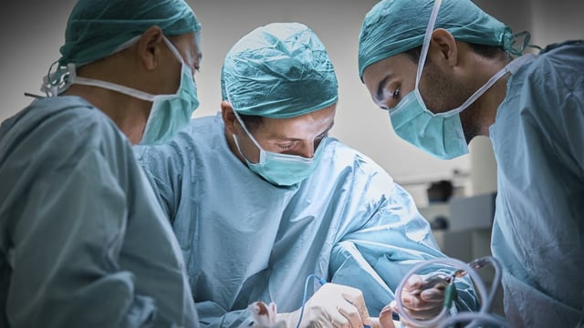 A photograph of 3 surgeons performing surgery on a patient.